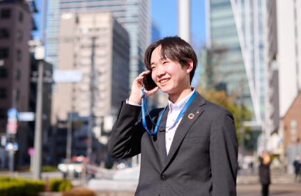 街中で電話をしながら微笑むスーツ姿の男性