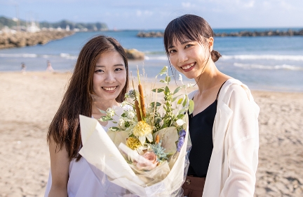 海辺で花束を持ち微笑む二人の女性
